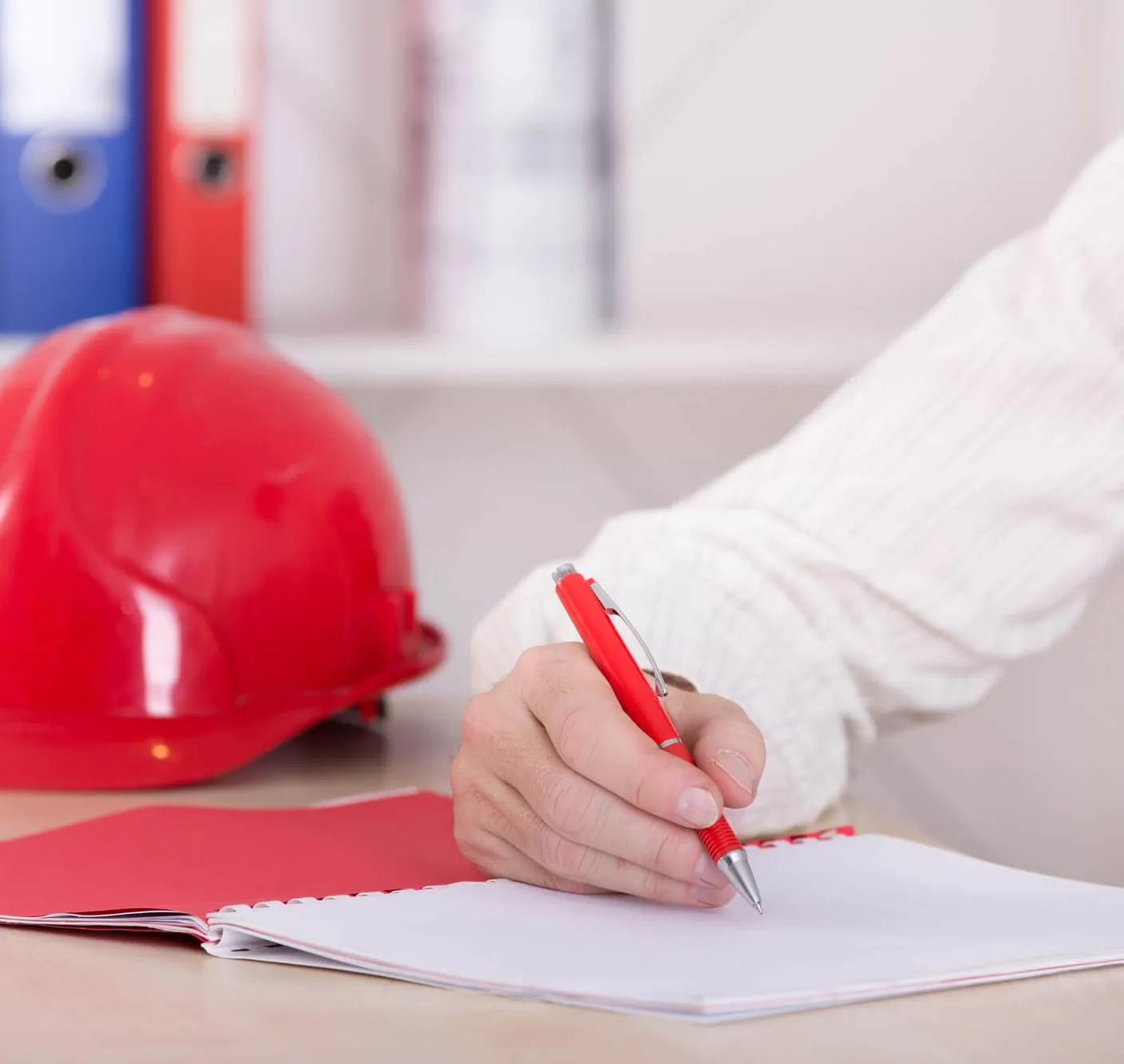 Hånd som skriver notater ved siden av en rød vernehjelm